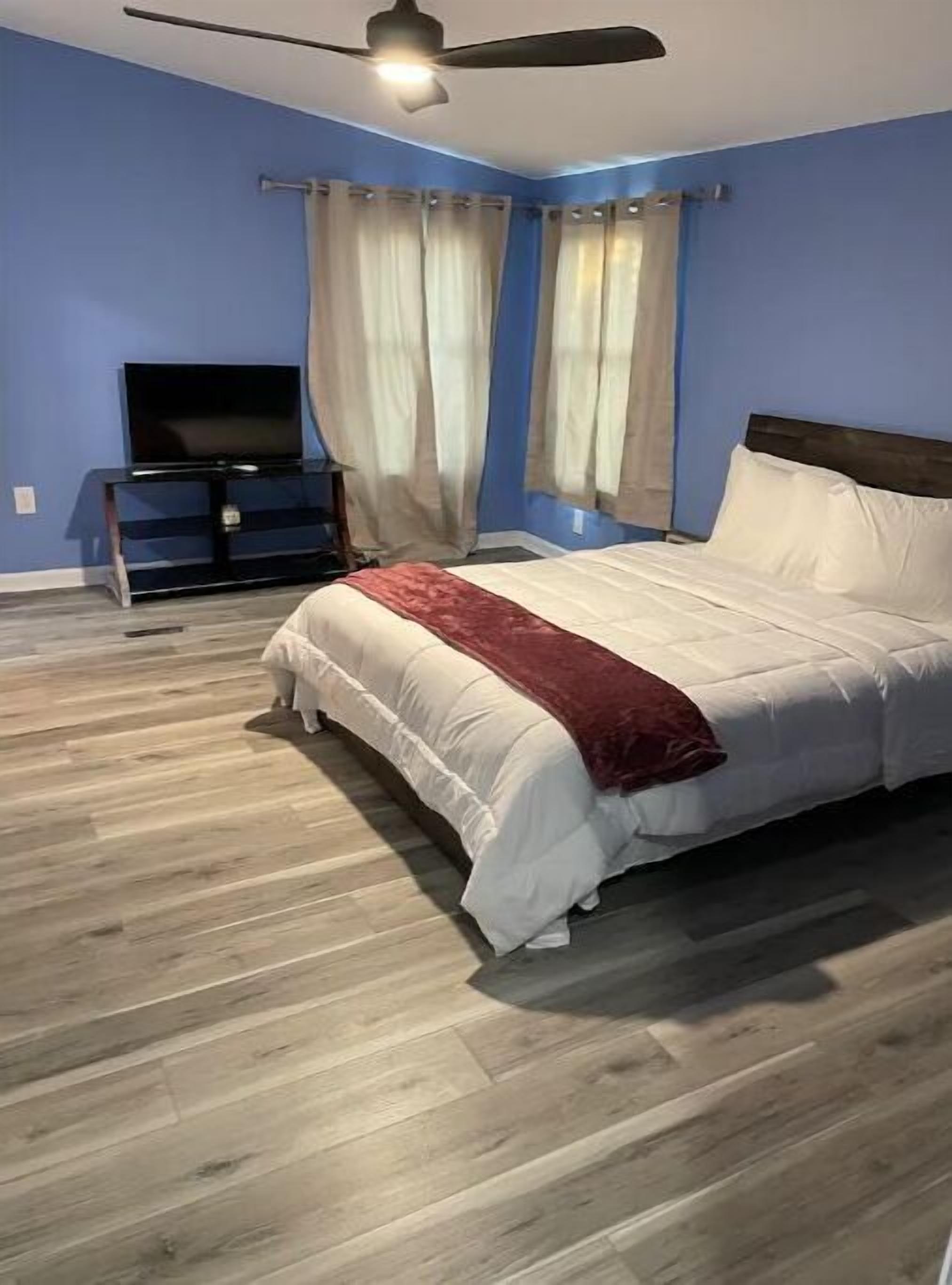 A bedroom with a bed, a TV on a stand, and a ceiling fan.