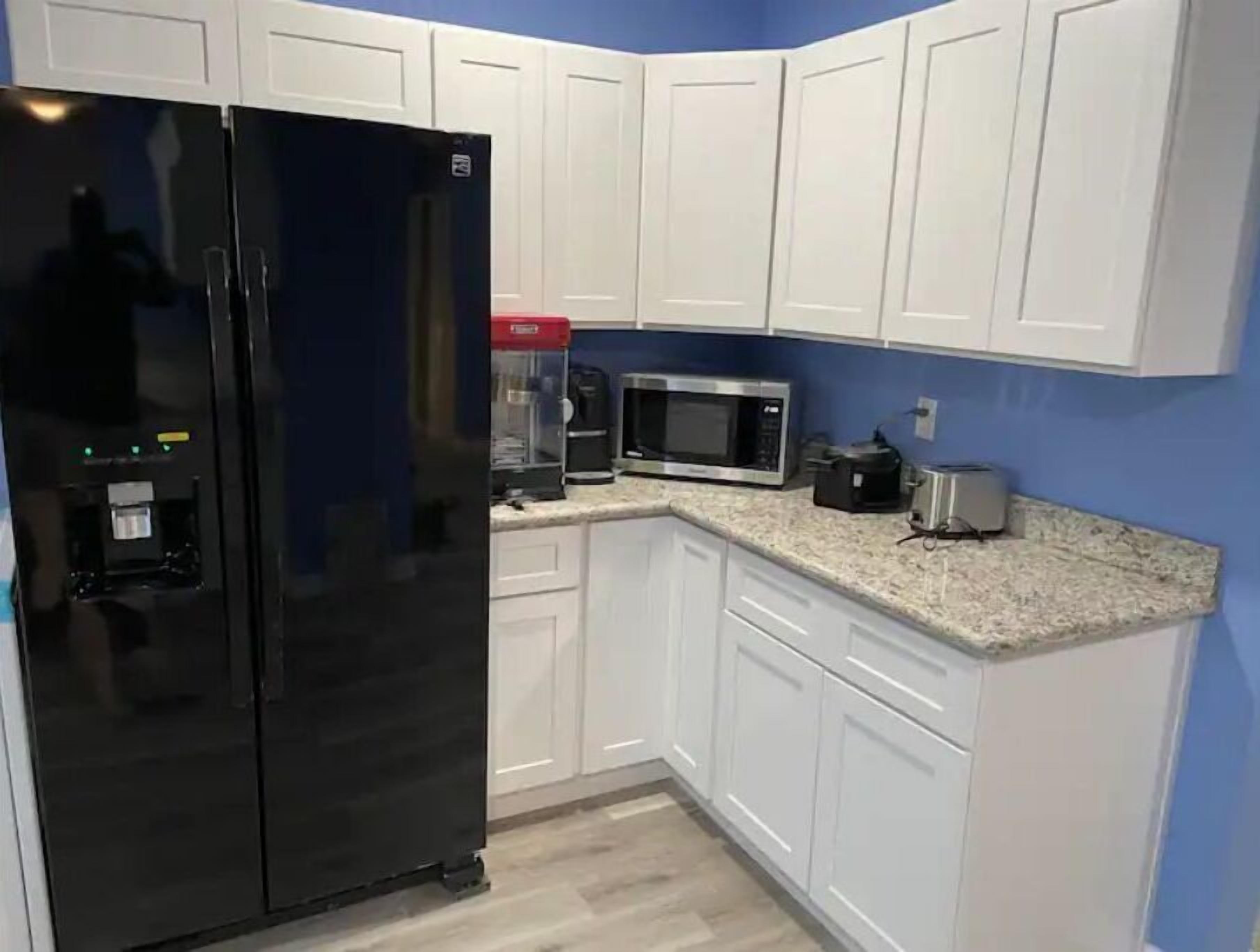 A kitchen with white cabinets, a black refrigerator, a microwave, and a coffee maker.