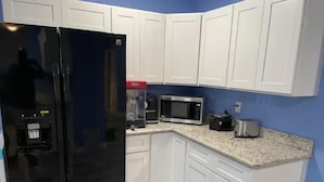 Una cocina con armarios blancos, un refrigerador negro, un microondas y una cafetera.