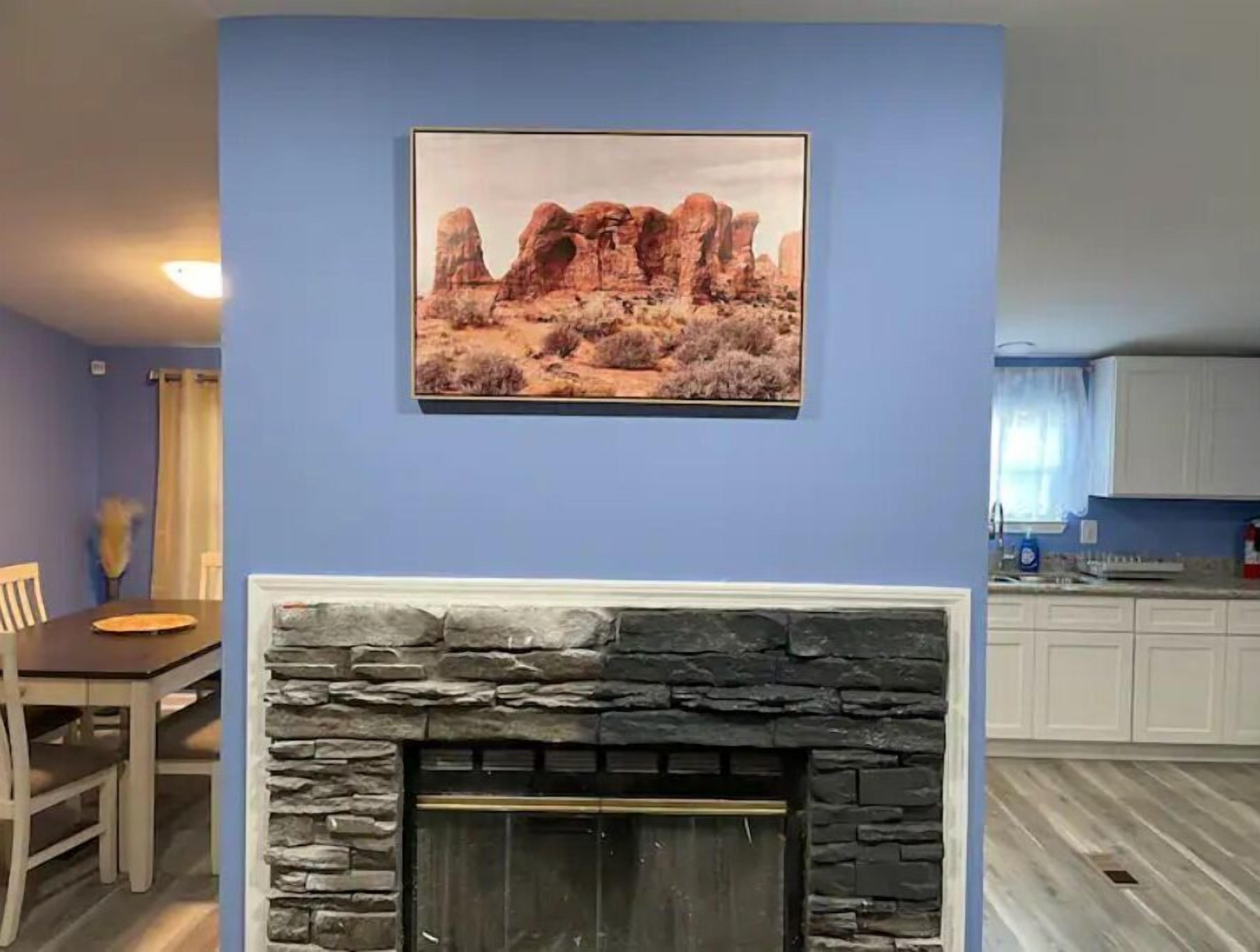A living room with a stone fireplace, a dining area with a table and chairs, and a kitchen in the background.