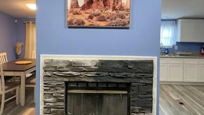 Una sala de estar con chimenea de piedra, un comedor con mesa y sillas, y una cocina al fondo.