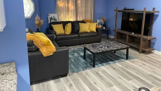 Una sala de estar con un sofá oscuro, una mesa de centro y un mueble para televisión.