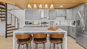 A modern kitchen with grey cabinets, a central island with bar stools, stainless steel appliances, and a wooden staircase. - Vashon Modern Beachfront Getaway: Pet & Family-Friendly with Stunning Views! (Vashon)