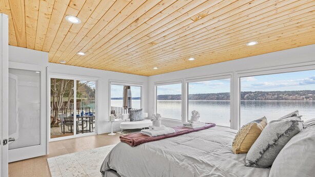 A bedroom with a large bed, a wooden ceiling, and a view of a lake. - Vashon Modern Beachfront Getaway: Pet & Family-Friendly with Stunning Views! (Vashon)