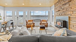 A cozy living room with a fireplace, comfortable seating, and a view through large windows. - Vashon Modern Beachfront Getaway: Pet & Family-Friendly with Stunning Views! (Vashon)
