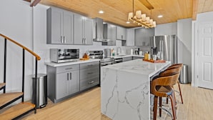 A modern kitchen with grey cabinets, stainless steel appliances, a marble island, and wooden bar stools. - Vashon Modern Beachfront Getaway: Pet & Family-Friendly with Stunning Views! (Vashon)