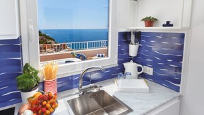 Une cuisine dotée d’un évier en acier inoxydable, d’un saladier rempli de fruits et offrant une vue sur la mer.