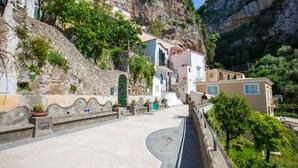 Une rue étroite bordée de bâtiments construits sur une colline, avec des murs en pierre et des plantes en pot.