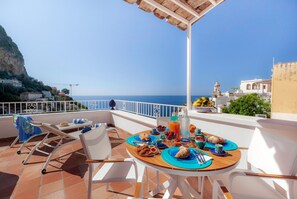 A terrace with a table set for breakfast, overlooking a coastal view with buildings and cliffs. - Medusa Positano (Positano)