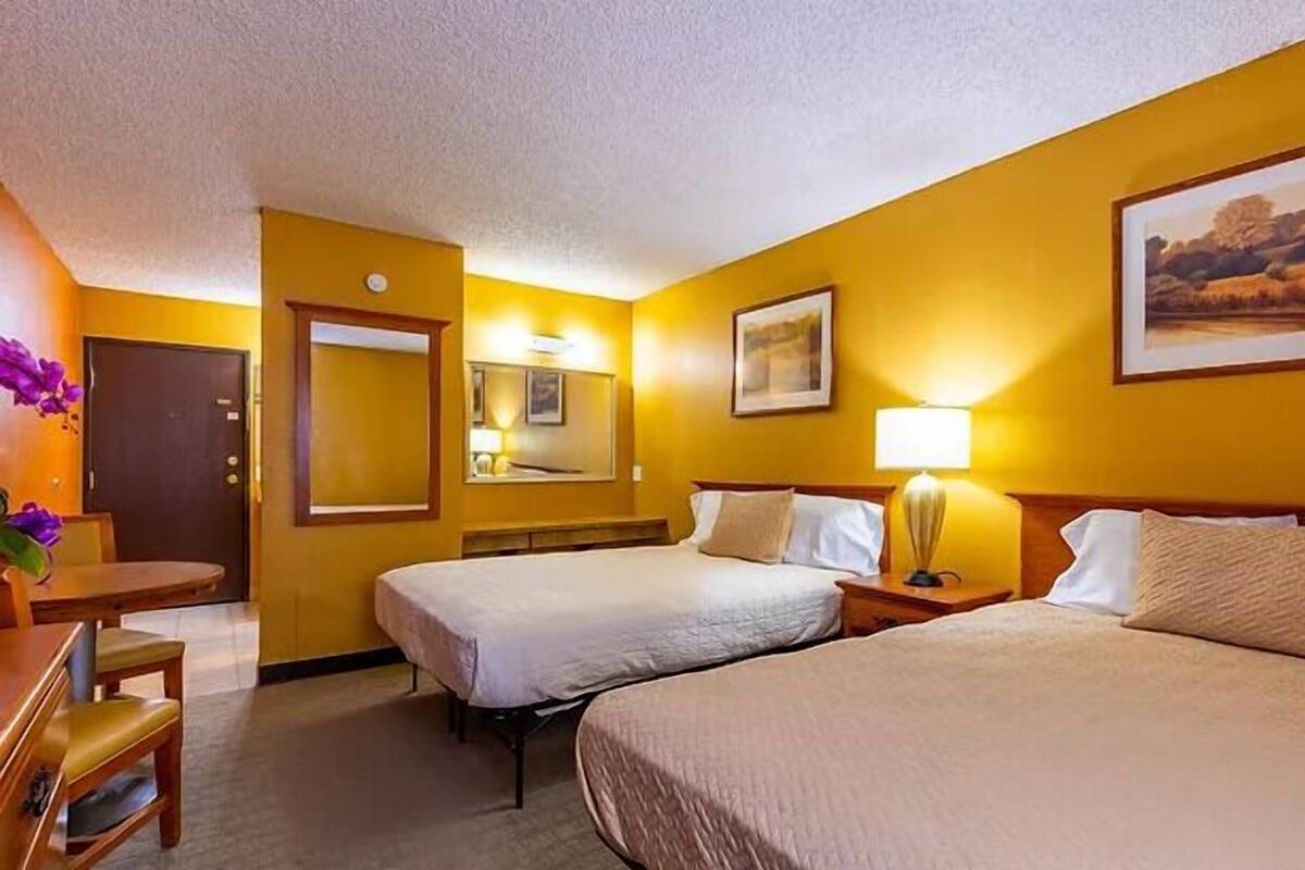 A hotel room with two beds, a desk, a chair, a lamp, and a painting on the wall.