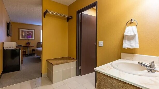 A compact bathroom with a sink, mirror, towel rack, and a door leading to another room. - Sun Valley Suites (Bullhead City)