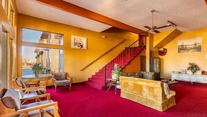 A spacious living room with a red carpet, a staircase, and a ceiling fan. - Sun Valley Suites (Bullhead City)