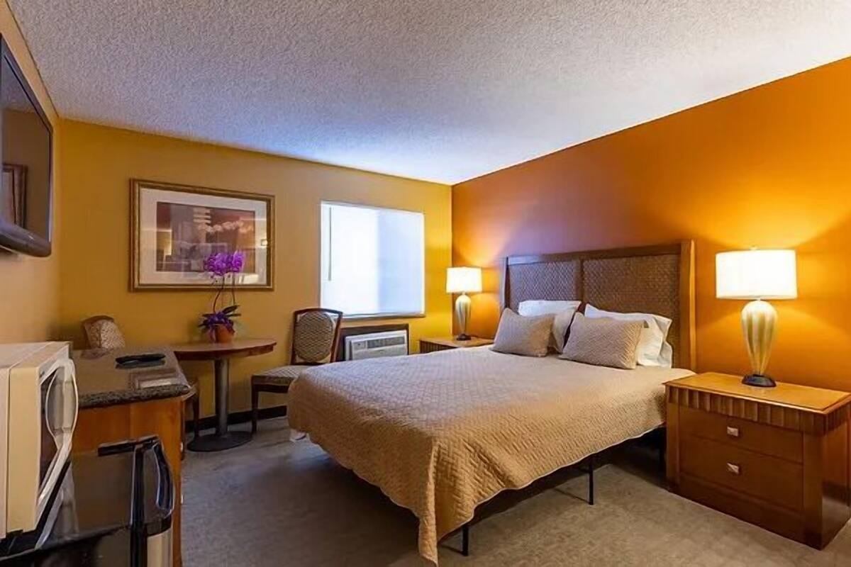 A hotel room with a bed, bedside tables, a desk, a chair, a small table with a lamp, and a picture on the wall.