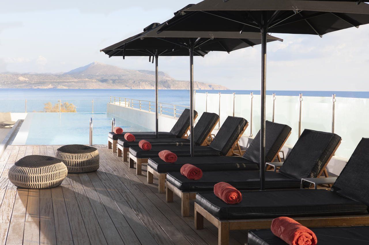A poolside area with lounge chairs and umbrellas, overlooking a body of water and a mountain.