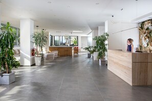 Un hall d’entrée spacieux avec un comptoir d’accueil, un espace salon et des plantes en pot.