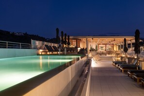 Ett område vid poolen med solstolar och parasoller, en pool och en byggnad med en fasad av glas.