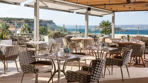 Un espace de restauration en plein air avec des tables et des chaises, une pergola et une vue sur la mer et les falaises.