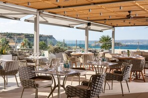 Un espace de restauration en plein air avec des tables et des chaises, une pergola et une vue sur la mer et les falaises.