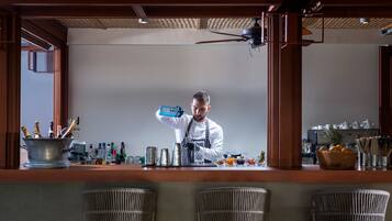 A bar area with a bartender preparing drinks, a coffee machine, and a variety of bottles and glasses on the counter.