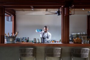 Un espace bar avec un barman préparant des boissons, une machine à café, et une variété de bouteilles et de verres disposés sur le comptoir.