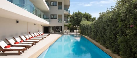 A modern hotel with a swimming pool, sun loungers, and a well-maintained garden.