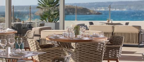 Un restaurante frente al mar con mesas redondas y sillas de mimbre.
