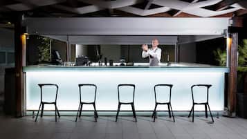 A modern bar with a long counter and five black chairs in front.