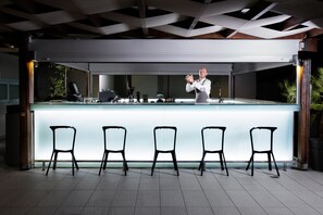 Eine moderne Bar mit einer langen Theke und fünf schwarzen Stühlen davor.