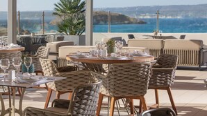 En restaurang vid havet med runda bord och stolar av rotting, med utsikt över havet.