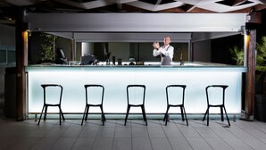 En modern bar med en lång bardisk och fem svarta stolar framför.