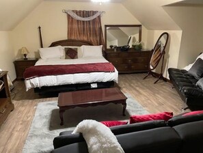 Quarto com cama grande, cômoda, espelho, sofá de couro preto e uma mesinha.