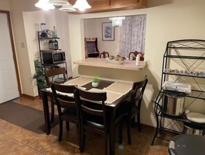 Uma cozinha compacta com mesa de jantar, cadeiras, micro-ondas, pequena geladeira e prateleira com potes.