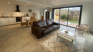 A modern living room with a brown leather sofa, a glass coffee table, and a dining area with white chairs. - New ! Family home, 5 minutes from the sea! (La Forêt-Fouesnant)