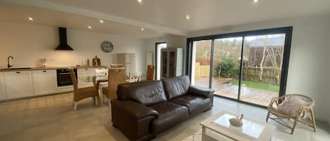 A modern living room with a brown leather sofa, a glass coffee table, and a dining area with white chairs.