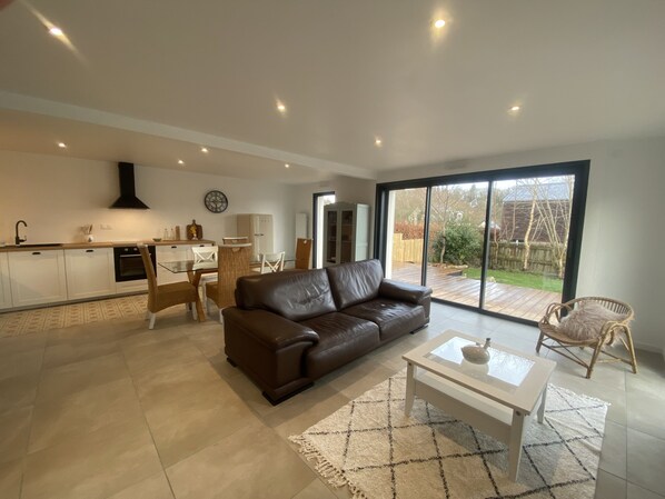 A modern living room with a brown leather sofa, a glass coffee table, and a dining area with white chairs. - New! Family home, just 5 minutes from the ocean! (La Forêt-Fouesnant)