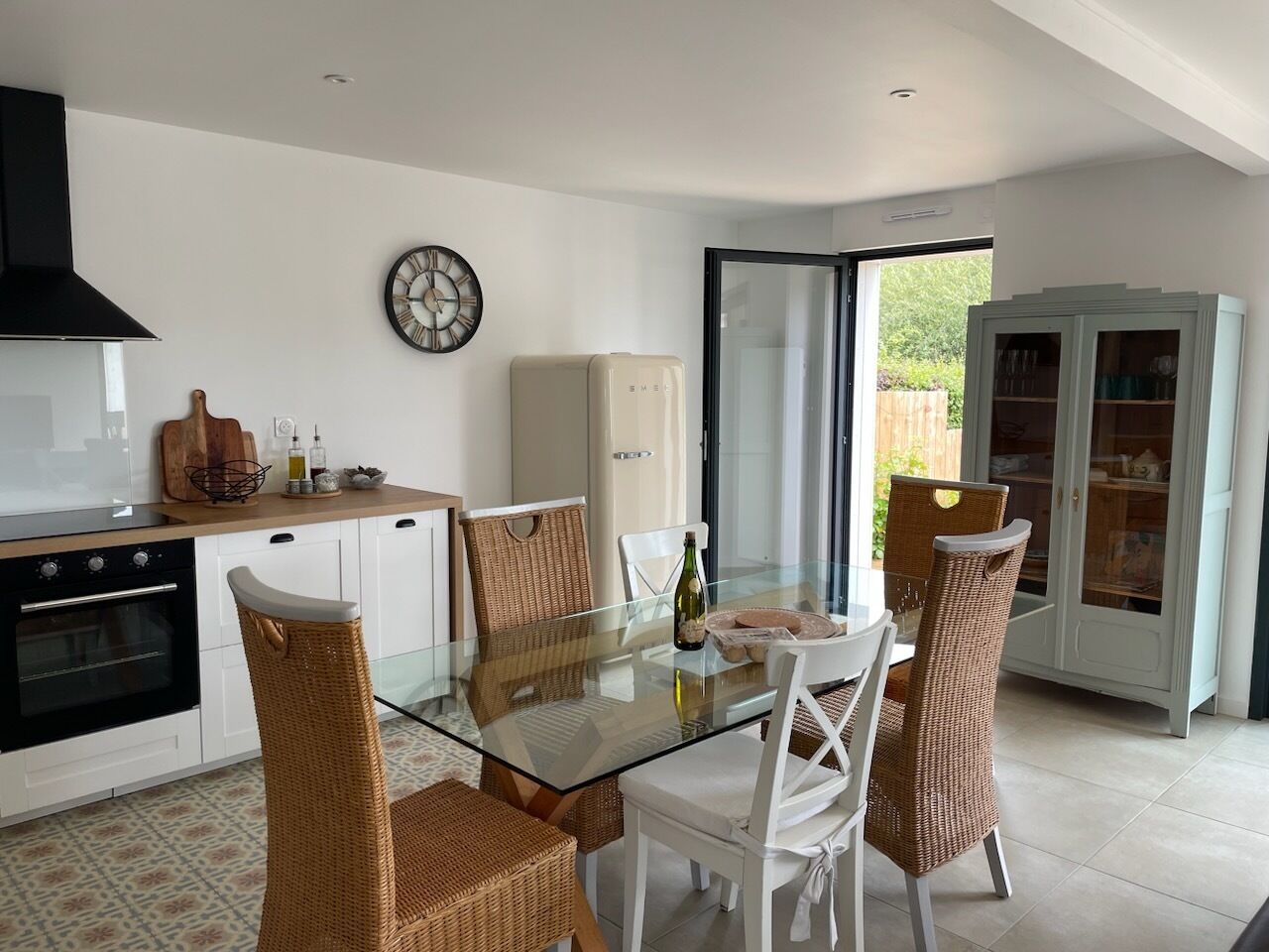 Une cuisine moderne avec une table à manger en verre, des chaises en osier et un four encastré.