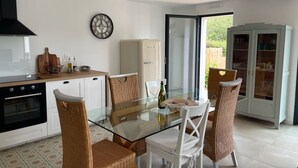 A modern kitchen with a glass dining table, wicker chairs, and a built-in oven. - New ! Family home, 5 minutes from the sea! (La Forêt-Fouesnant)