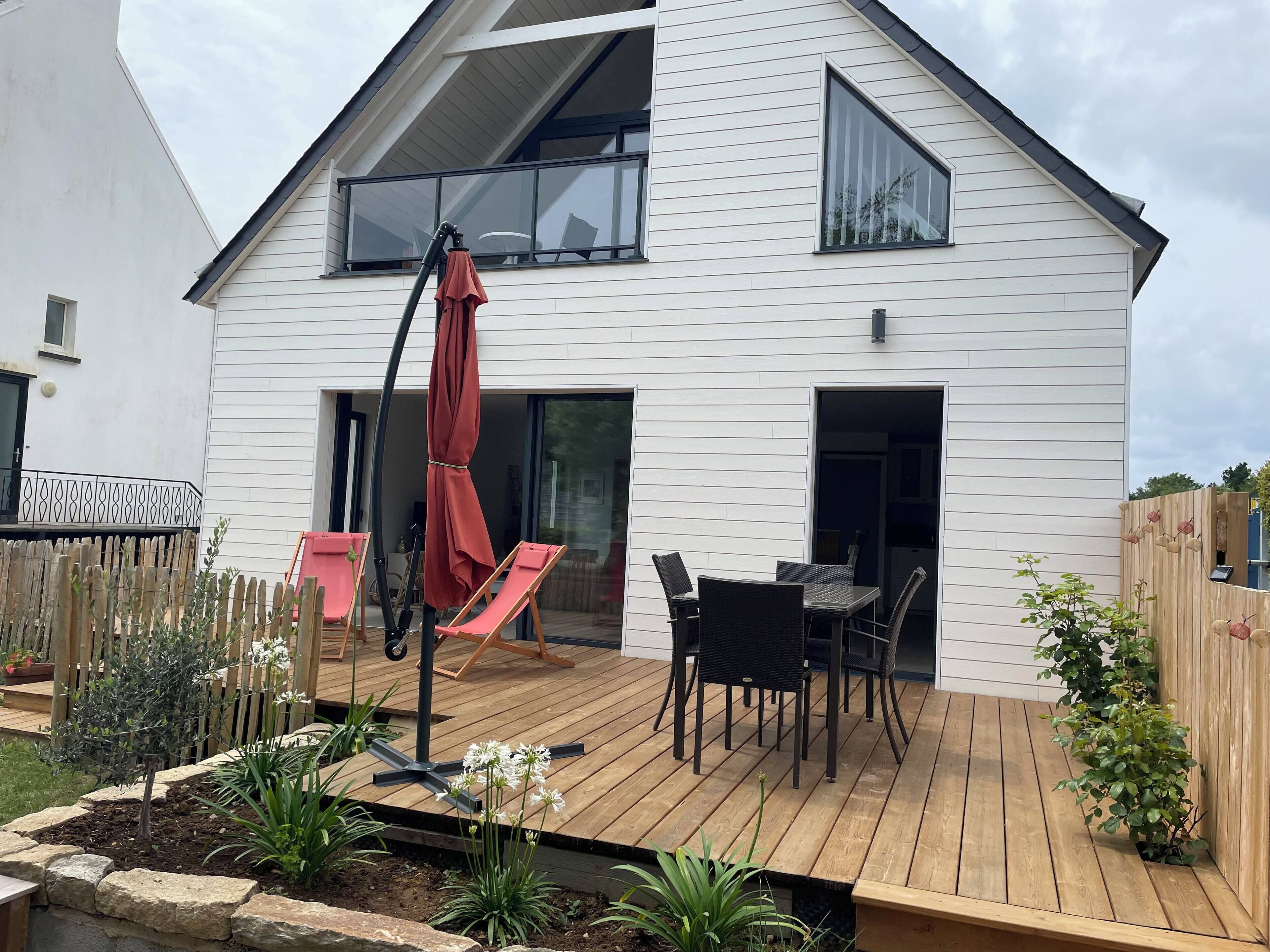 A modern two-story house with a wooden deck, outdoor seating, and a garden.