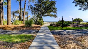 A wooden pathway leading to a beach area with a wooden fence and a lamp post. - Relaxing Poolside Condo Steps from the Beach (Hilton Head Island)