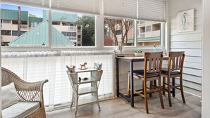 A cozy room with a wicker sofa, a small table with chairs, and a large window with blinds. - Relaxing Poolside Condo Steps from the Beach (Hilton Head Island)