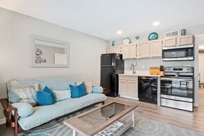 Cocina moderna con refrigerador, microondas y horno. Hay un sofá azul claro con cojines azules y una mesa de centro de madera.