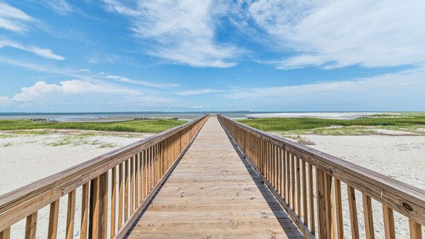 A wooden boardwalk leading to a beach with grassy dunes and a clear blue sky. - Relaxing Poolside Condo Steps from the Beach (Hilton Head Island)
