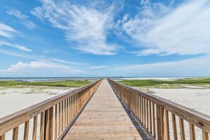 A wooden boardwalk leading to a beach with grassy dunes and a clear blue sky.