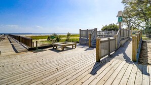 A wooden deck with a bench and a table, overlooking a beach. - Relaxing Poolside Condo Steps from the Beach (Hilton Head Island)
