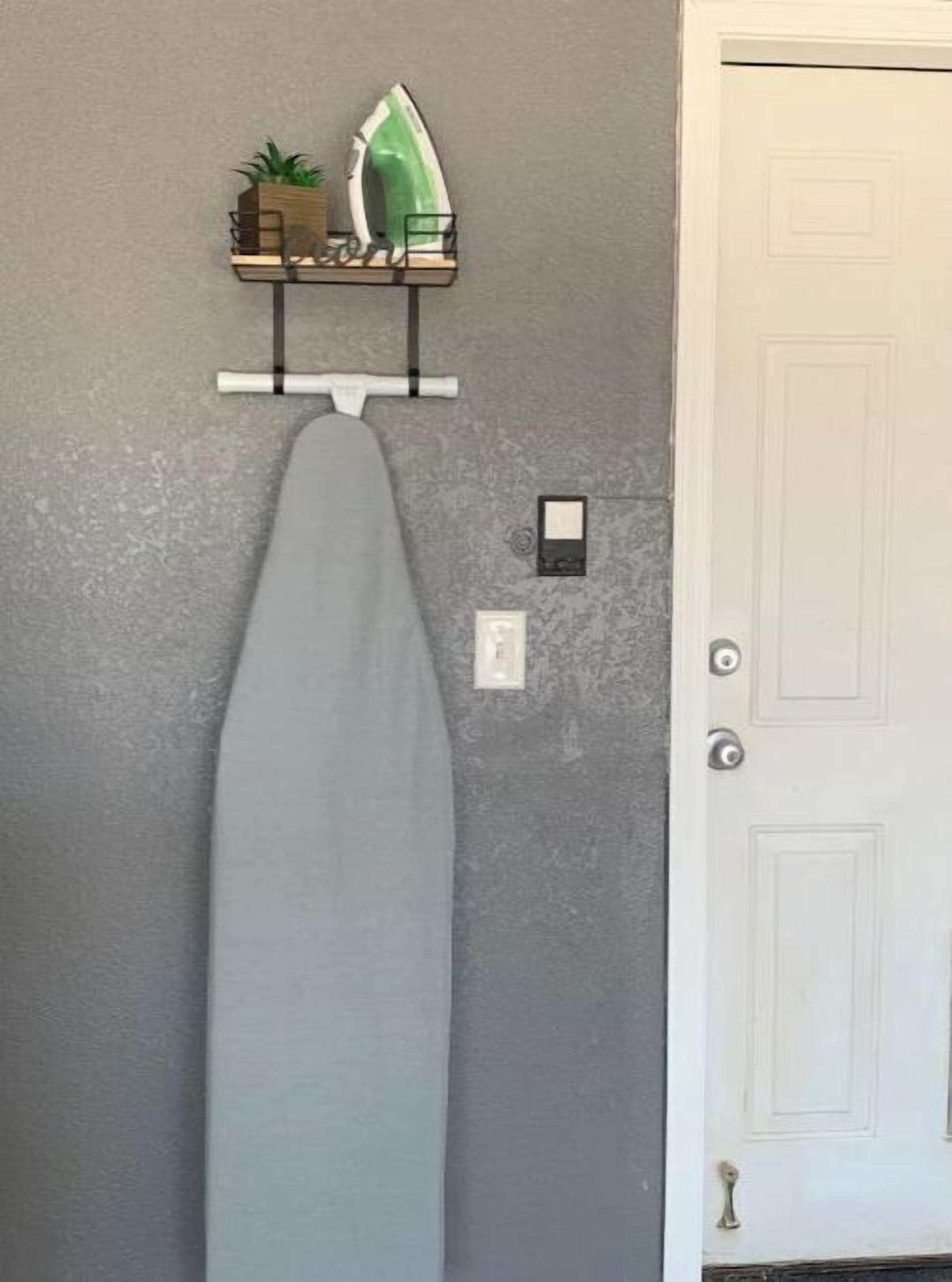 Ein an der Wand montiertes Bügelbrett mit Bügeleisen und einem kleinen Regal darüber.
