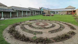 Une cour avec un jardin en spirale, des bâtiments en pierre et un banc en bois.