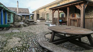 Un espace extérieur rustique avec un sol en pierre, des bancs en bois et un coin salon abrité.