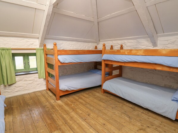 A room with two bunk beds, wooden flooring, a green curtain, and a white textured wall.