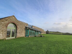 A stone building with a green door and windows, a grassy lawn, and a stone wall in the background.