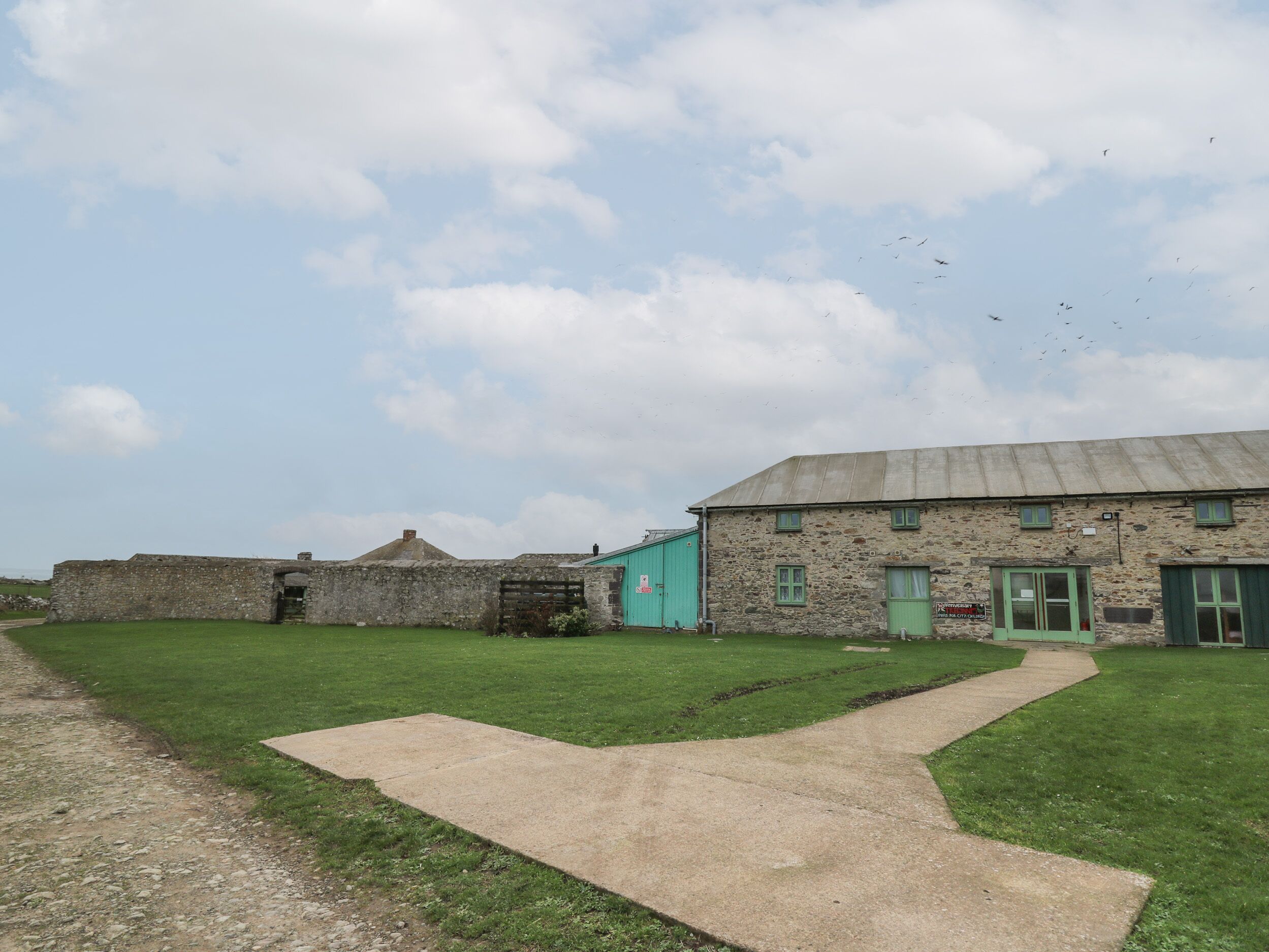 A stone building with a green door and windows, a paved path, and a grassy area.